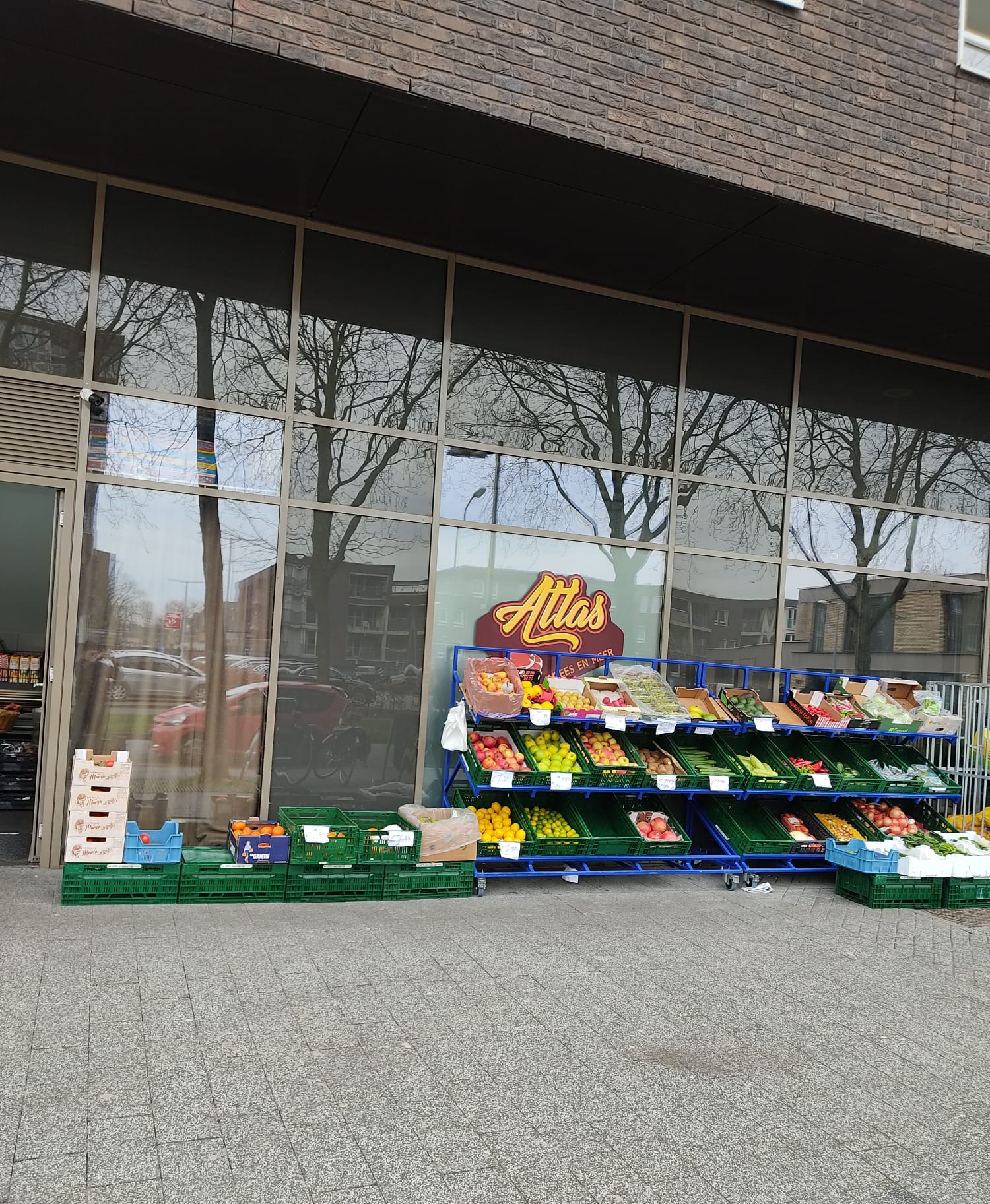 De winkel van buiten, met de rekken groente en fruit langs de pui
